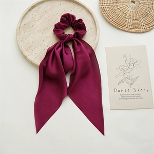 Close-up of deep red satin hair scrunchie with long ribbon bow on marble stone tray