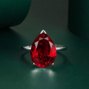 Pear cut red ruby ring in silver setting with adjustable band on green background