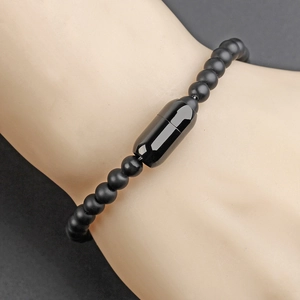 Men's beaded bracelet with matte black beads and a polished capsule clasp on a wrist