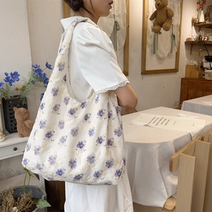 Close-up of a white canvas tote bag featuring purple floral embroidery and lace texture