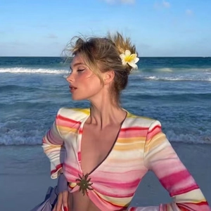 Close-up of a striped beach crop top featuring a golden sun-shaped metal buckle accessory