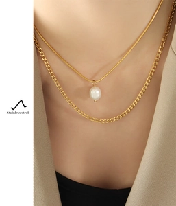Detail of layered stainless steel necklace with gold curb chain and pearl pendant