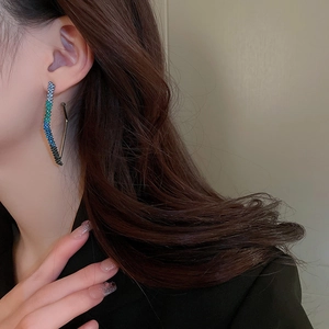 Close-up of S-curve dangle earrings with blue-green gradient rhinestones on model