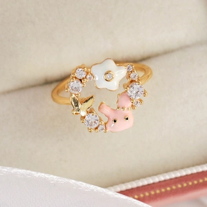 Close-up of golden ring with white enamel flower, pink rabbit and zircon stones