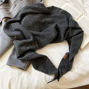 Texture de tricot d'une écharpe triangle gris foncé avec écusson en cuir marron