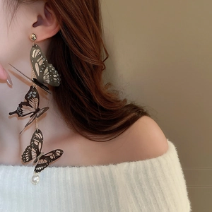 Détail de boucles d'oreilles pampilles avec papillons en acrylique noir et perle blanche