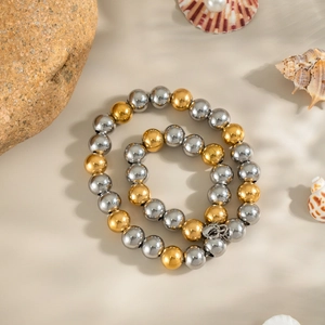 Elegant gold and silver two-tone beaded necklace arranged in a spiral on natural rocks