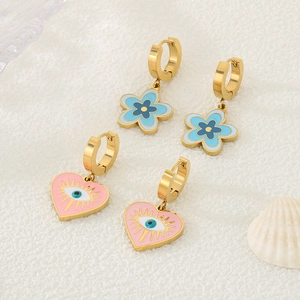 Boucles d'oreilles fleur dorée et cœur rose mauvais œil présentées avec des coquillages