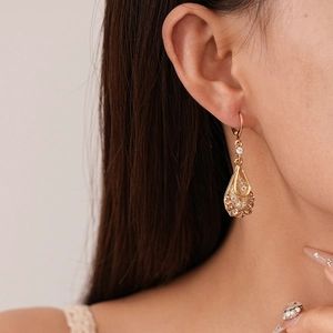Macro detail of gold-tone teardrop earrings with champagne zircons on a model