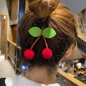 Detailed view of sweet cherry hair clip with red plush balls and green felt leaves