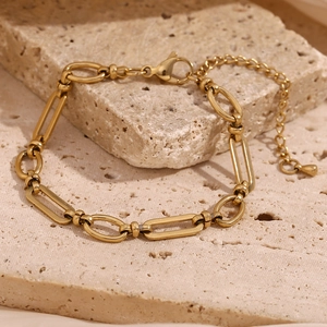 Detail of 14K gold plated paperclip chain bracelet on a textured beige stone background