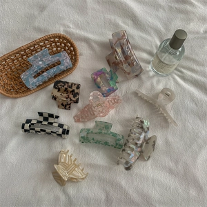 Assorted acetate hair claws featuring marble patterns and checkered designs on beige fabric