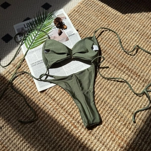 Nahaufnahme des olivgrünen Glitzer-Bikinis auf Strohmatte mit Strandzubehör