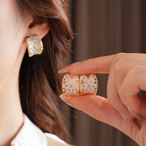 Détail d'une boucle d'oreille fleurie en forme de C dorée, blanche et rose portée
