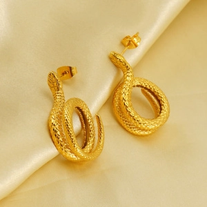Macro view of gold snake-shaped earrings with scale texture on soft yellow silk