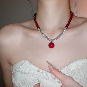 Detail of elegant red beaded necklace with zircon accents on a white lace blouse model