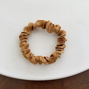 Close-up of golden brown satin scrunchie with silk texture on a white plate and wood background