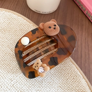 Detail of tortoiseshell hair clip featuring velvet bears and a pearl on a ceramic plate