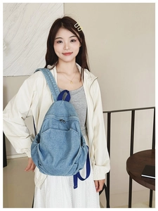 Close-up of a vintage blue denim backpack with zipper pockets on a female model