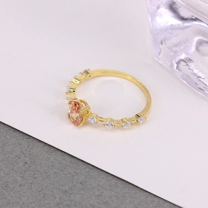 Detail of gold ring featuring an oval orange gemstone and small round zircon accents