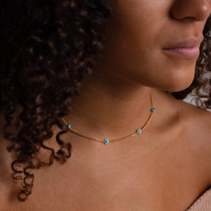 Close-up of turquoise pendant necklace on a gold chain worn as a choker by a model