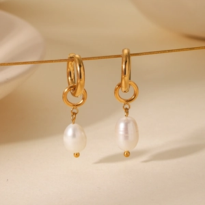 Close-up of gold hoop earrings with white baroque pearls on a minimalist background