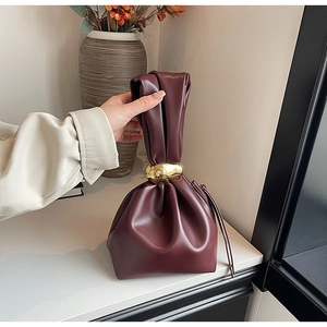Close-up of burgundy leather bucket bag with elegant pleats and golden metal buckle details