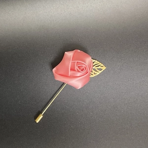 Macro shot of pink satin rose lapel pin with gold leaf and long needle on grey background