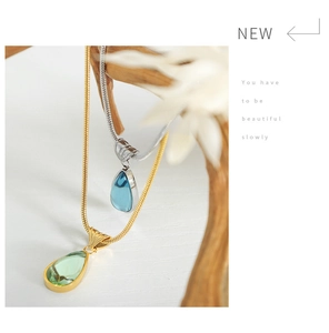 Detailed shot of green and blue teardrop pendants on sleek snake chains and wood stand