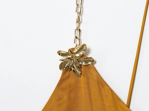Detail of golden metal flower charm and thin chain strap on ginger satin midi dress