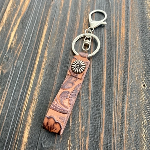 Close-up of Western-style embossed brown leather keychain with sunflower rivet and lobster clasp