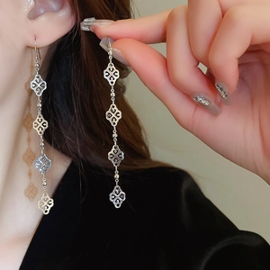Boucles d'oreilles pendantes argentées avec trèfles évidés et pompons sur un mannequin