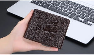 Close-up of a brown alligator embossed men's bifold wallet held by hand in office setting