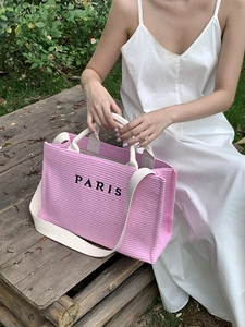 Pink woven Paris tote bag with white shoulder straps carried by a model in a summer dress