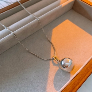 Close-up of a silver spherical pendant on a delicate steel chain in a velvet jewelry box
