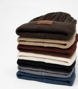 Dettaglio di berretti in maglia spessa impilati in vari colori con etichetta in pelle