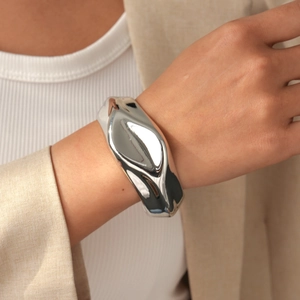 Close-up of irregular silver fluid bangle paired with a beige blazer for a modern look