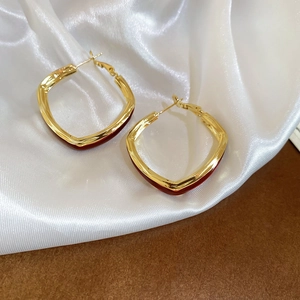 Close-up of gold V-shaped hoop earrings with red enamel on a white silk background
