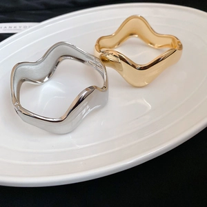 Detailed close-up of wavy gold and silver open bangles with high-polished mirror finish