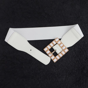 Detail of a white elastic belt featuring a geometric gold and white square buckle