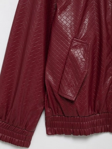 Close-up of burgundy woven faux leather bomber jacket showing elastic hem and side pocket