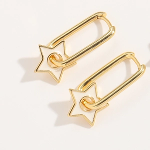 Close-up of golden safety pin earrings with white enamel star charms in minimalist style