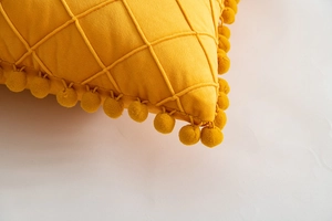Detail of yellow velvet pillow with diamond lattice texture and soft pom-pom fringe edges
