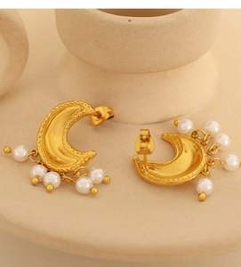 Makroaufnahme von goldenen Halbmond-Ohrringen mit eleganten weißen Perlenquasten und Textur