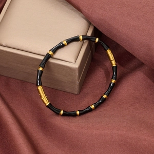Detail of bamboo-style black enamel bracelet with gold-plated metal spacers on silk