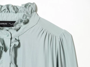 Detail of ruffle stand collar and pleated shoulder on light green viscose top