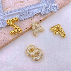 Close-up of gold copper letter pendants Z A F S with cubic zirconia inlay on beige plaster