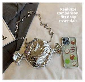 Detailed view of silver candy-shaped evening bag with chain strap next to a phone