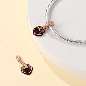 Macro view of heart charm in rose gold with red enamel and ribbon detail on snake chain