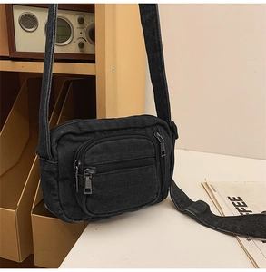 Detail of black washed denim crossbody bag featuring multi-pocket zippers on a wooden shelf